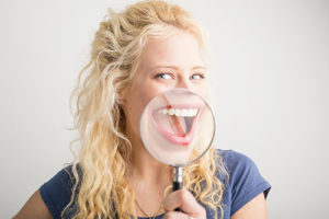 a woman smiling through a magnifying glass after getting dental bonding in missouri city tx