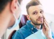 patient who is seeking treatment for emergency dental services holding his mouth in pain