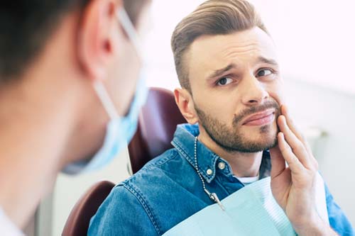emergency-dental-services patient who is seeking treatment for emergency dental services holding his mouth in pain
