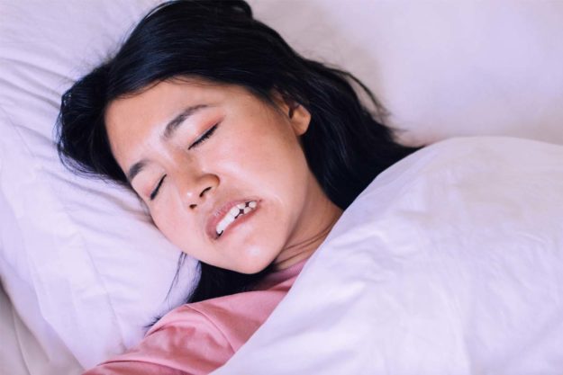 symptoms-of-teeth-grinding woman sleeping showing symptoms of teeth grinding